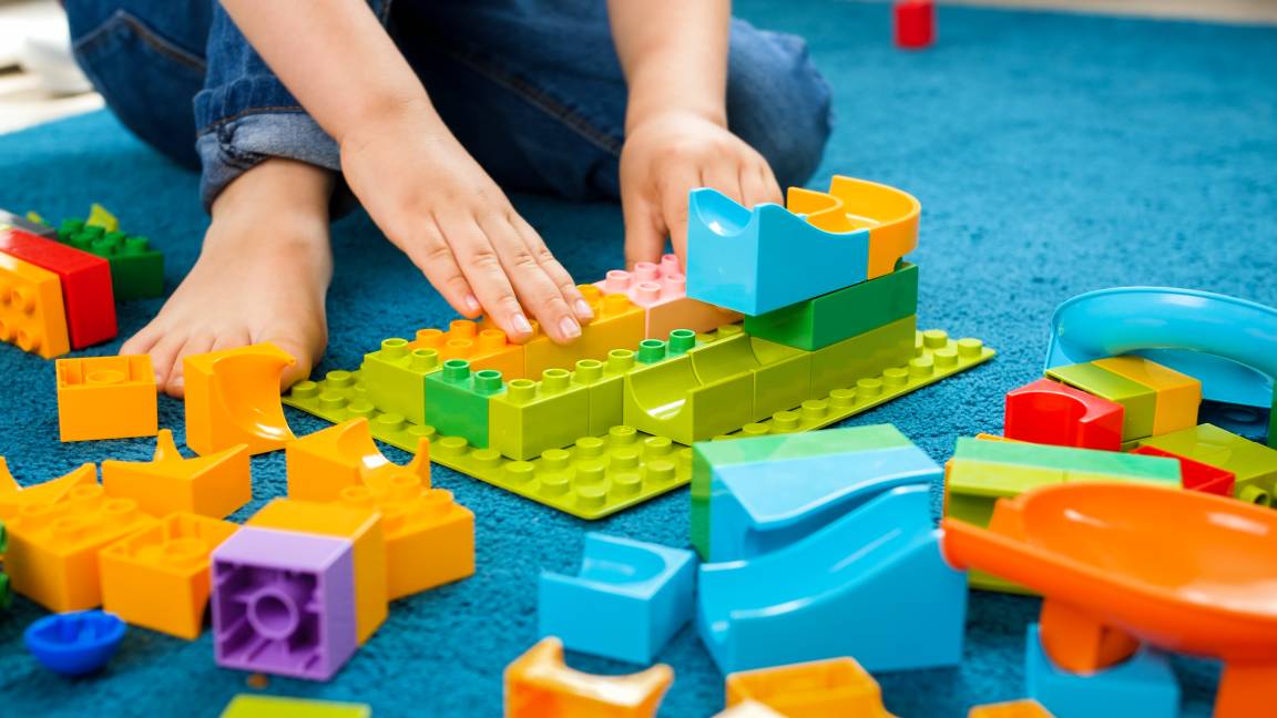 Primeiro plano de uma criança pequena sentada no tapete de casa a brincar com blocos coloridos