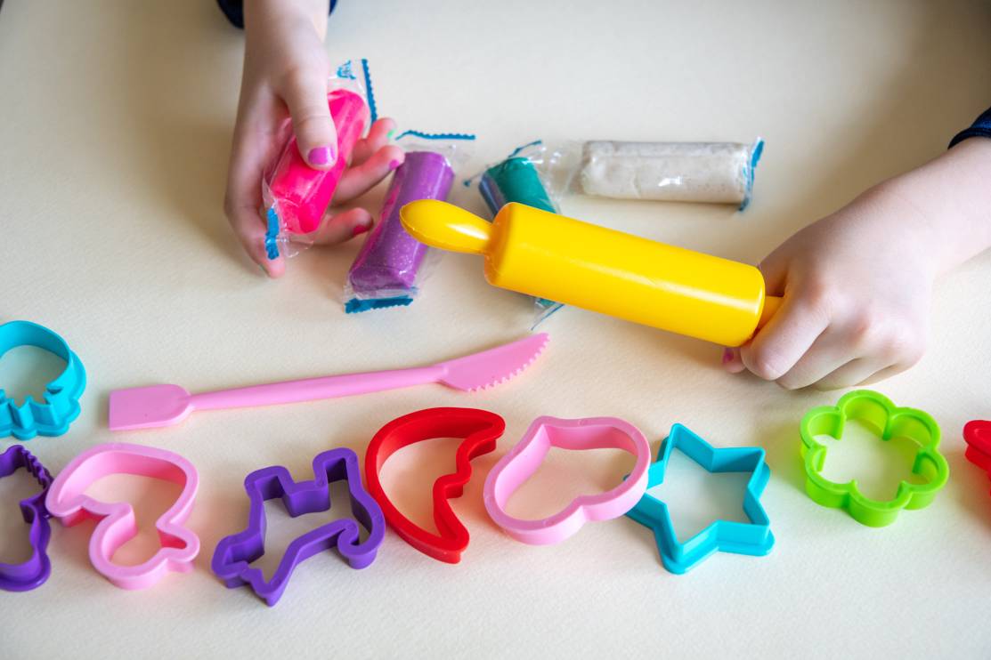 Mãos de criança a brincar com plasticina colorida, utilizando moldes de plástico e um rolo amarelo