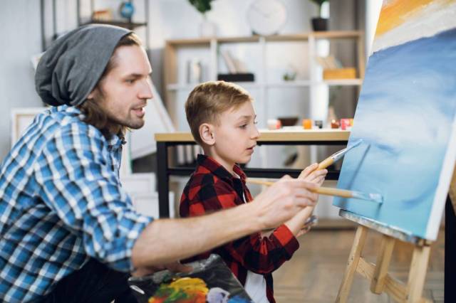 A boy and his father painting with brushes on canvas