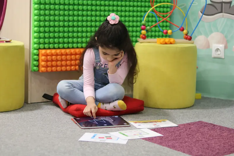 Young girl independently engaged with Magrid visual cognitive learning on tablet with printed activity cards