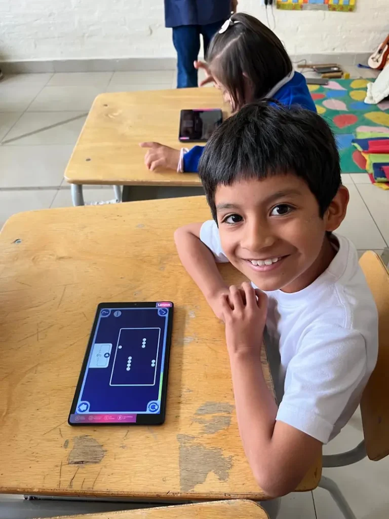 Un garçon souriant dans une classe inclusive, utilisant la méthode de développement cognitif visuel sans langage de Magrid sur une tablette
