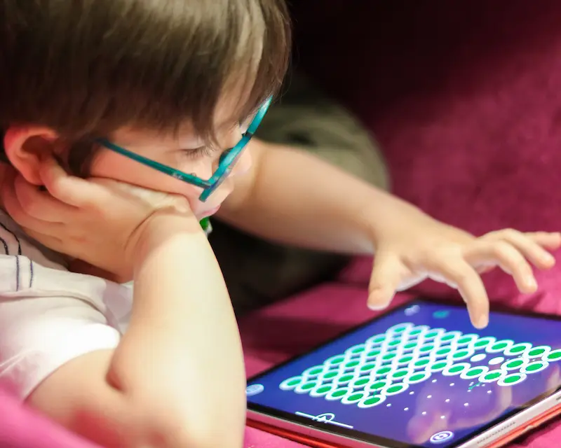 Niño con gafas, totalmente concentrado en una actividad de desarrollo cognitivo visual de Magrid en una tableta, en un entorno tranquilo y adaptado a las necesidades sensoriales.