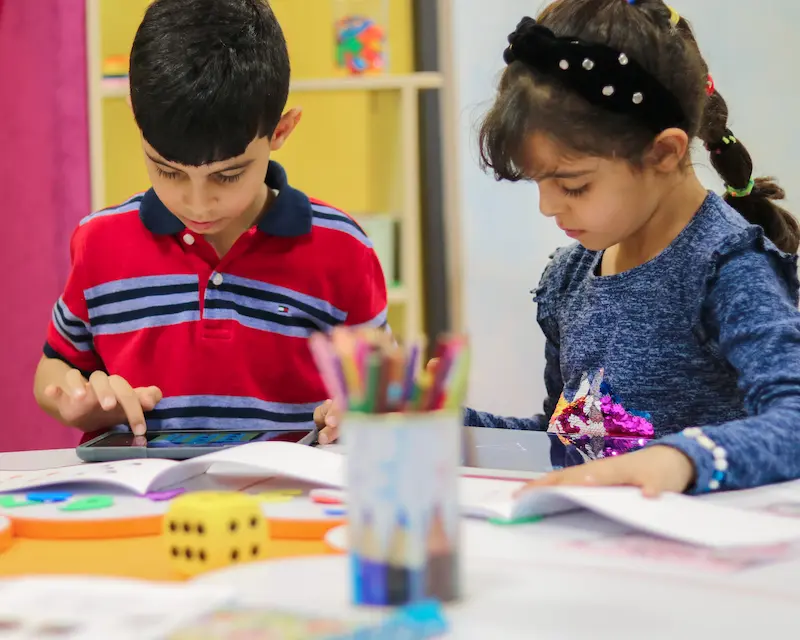 Dos niños participaban por separado en las actividades de desarrollo cognitivo visual y en los materiales didácticos de Magrid en una mesa.