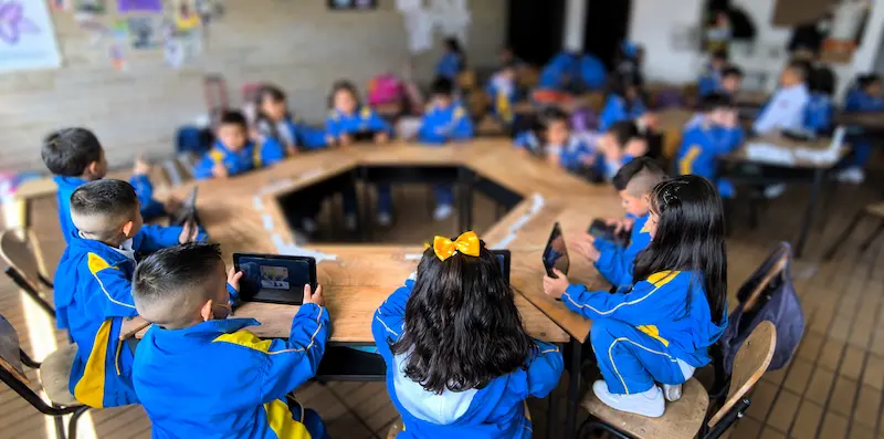 Uma turma inteira de crianças fardadas a utilizar tablets com o Magrid numa sala de aula disposta em círculo, na Colômbia