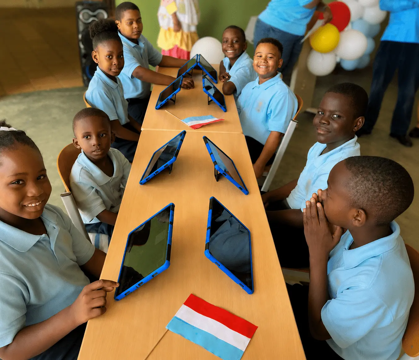 Kinder in einem Magrid-Lernzentrum auf Curaçao lernen mit Tablets und luxemburgischen Flaggen auf dem Tisch